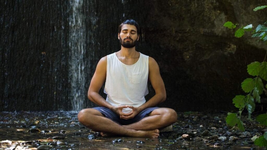 Hombre meditando en el bosque con una cascada de fondo