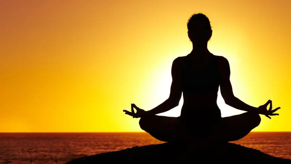 sombra de persona meditando y de fondo esta la puesta de sol